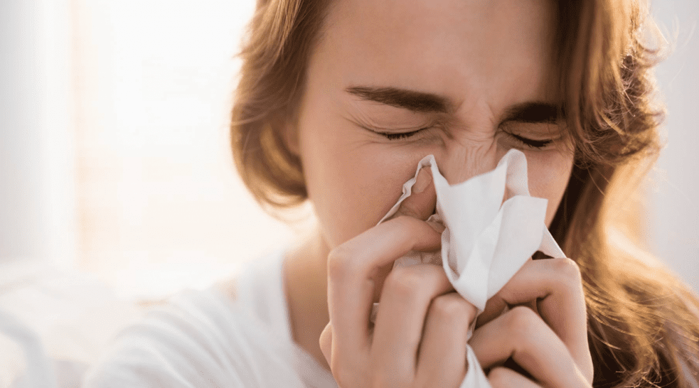 young woman with colds blowing her nose to a tissue paper